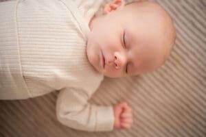 A peacefully sleeping baby dressed in white lies comfortably on striped fabric during newborn session.