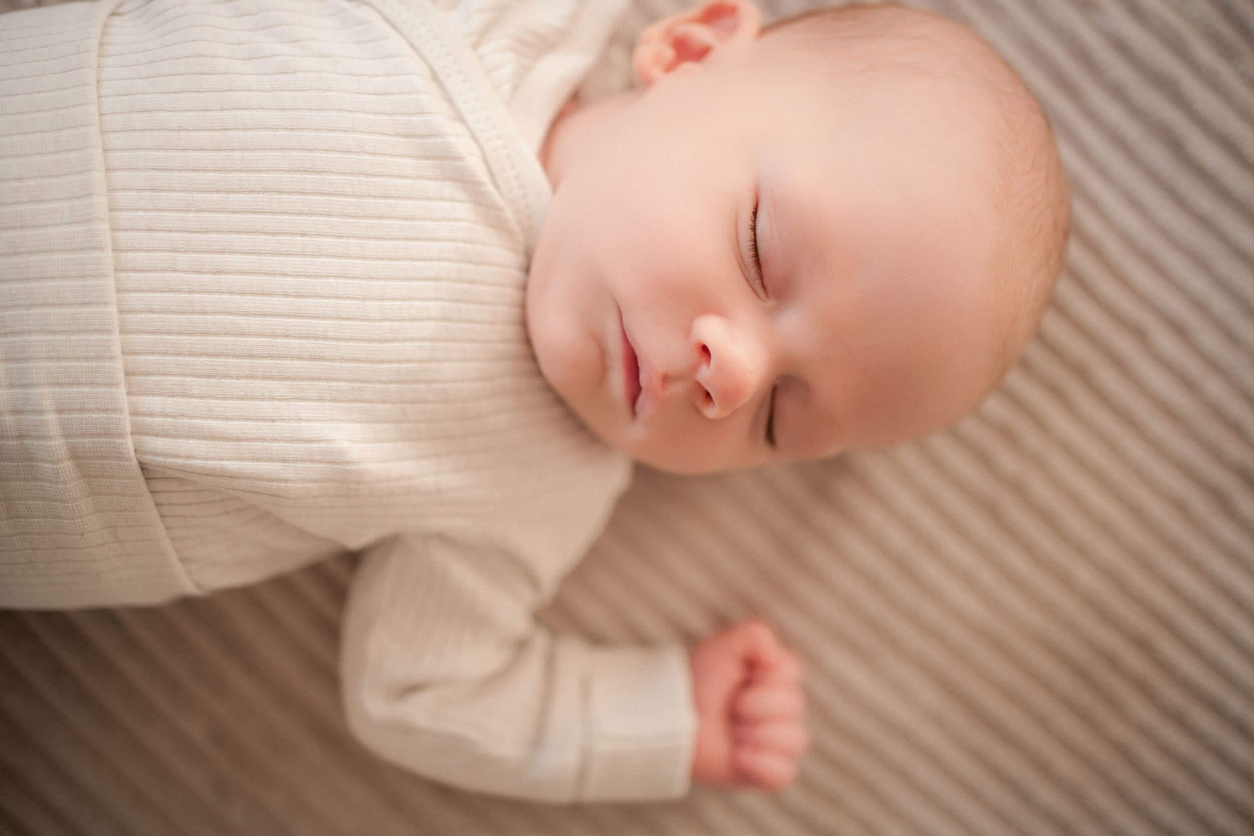 A peacefully sleeping baby dressed in white lies comfortably on striped fabric during newborn session.