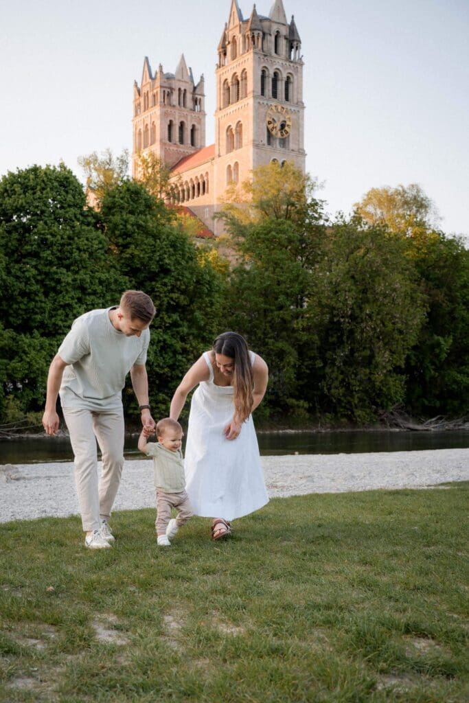 Family sharing playful moment on lawn near sunlight church along the Isar in Munich.