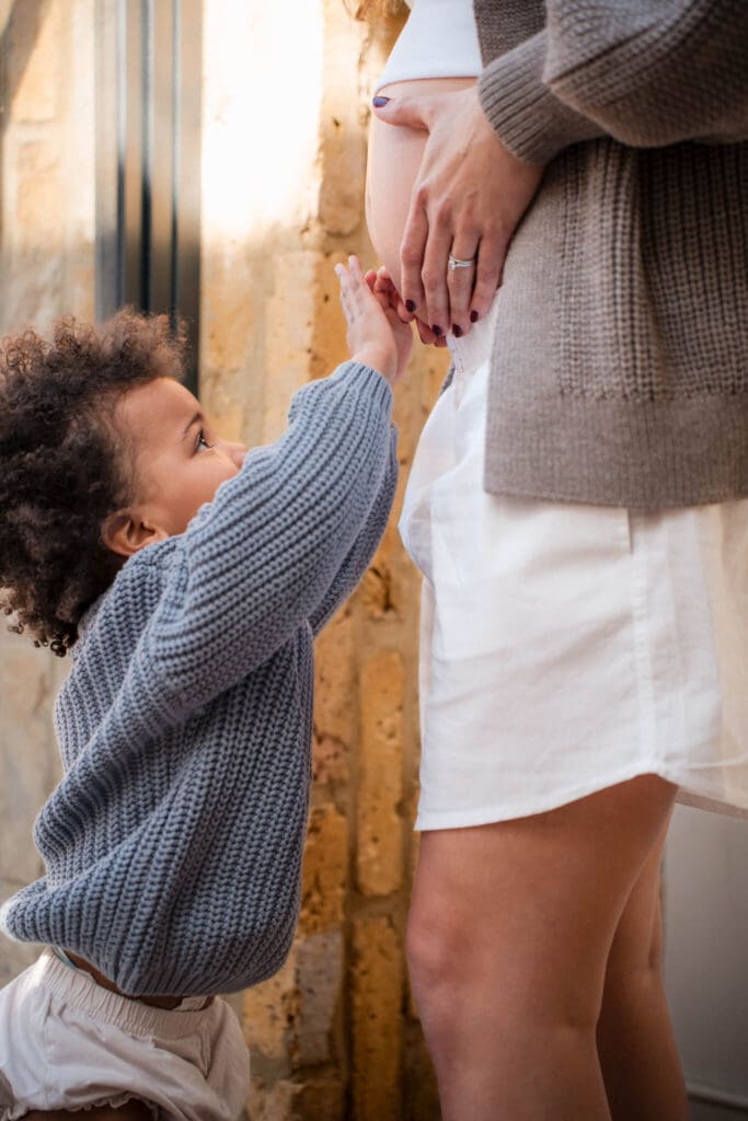 Young toddler reaches up to touch mom's pregnant belly during maternity photoshoot in Munich