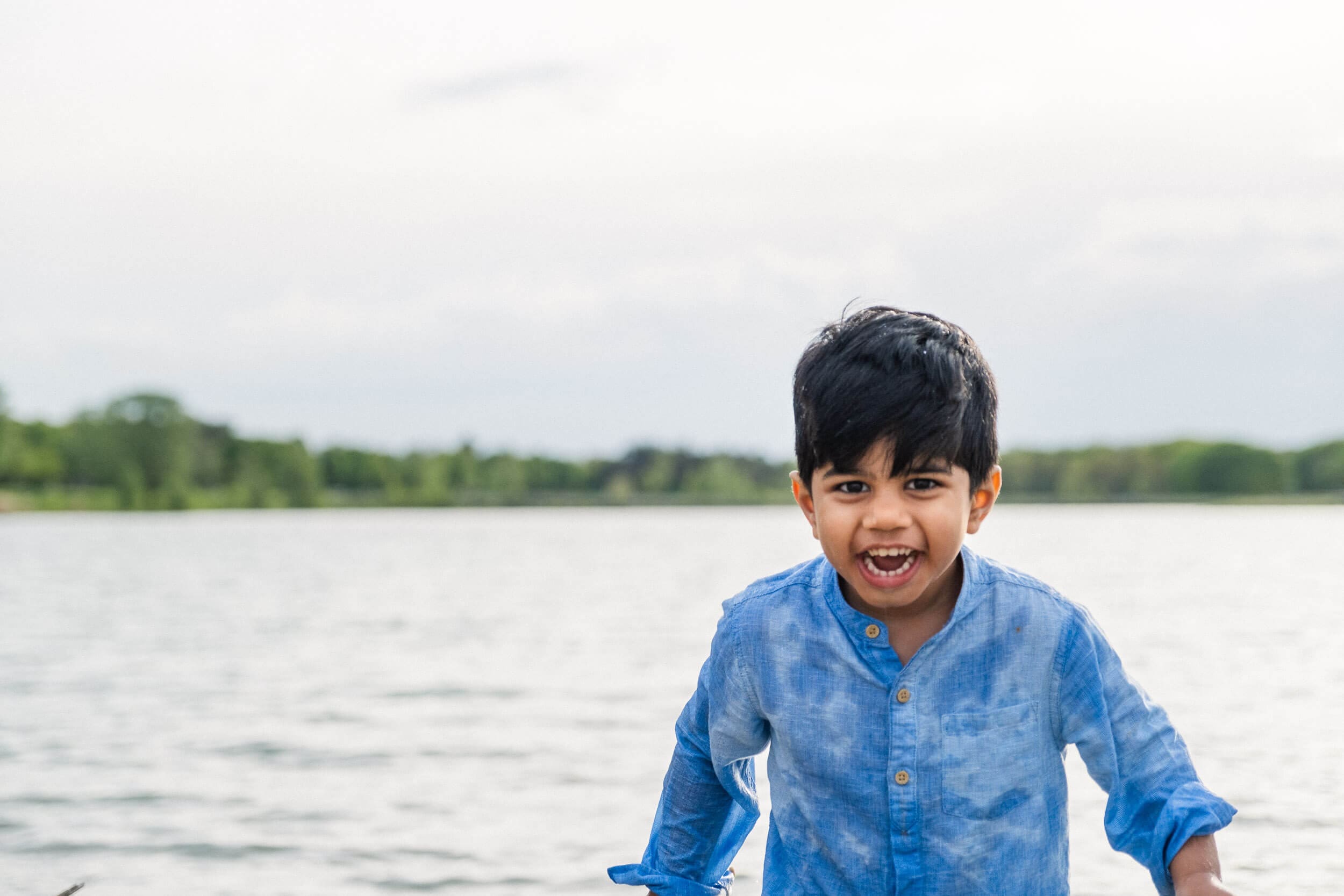 Young boy laughs in front of a lake with water soaking his shirt from splashing