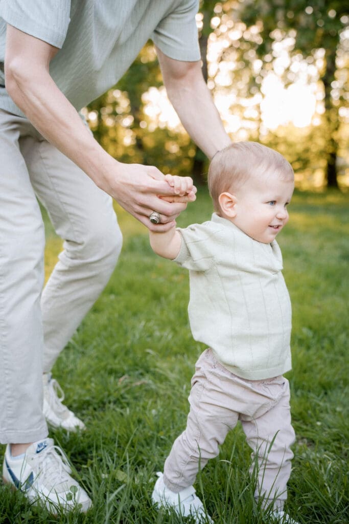 Three sequential photos showing supportive hands guiding a small child learning to walk on green grass during golden hour.