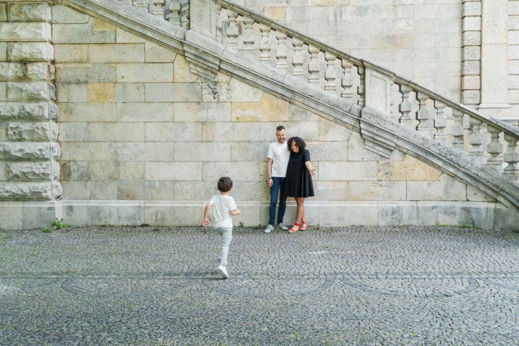 Young boy runs to his parents while mom opens her arms to embrace him.