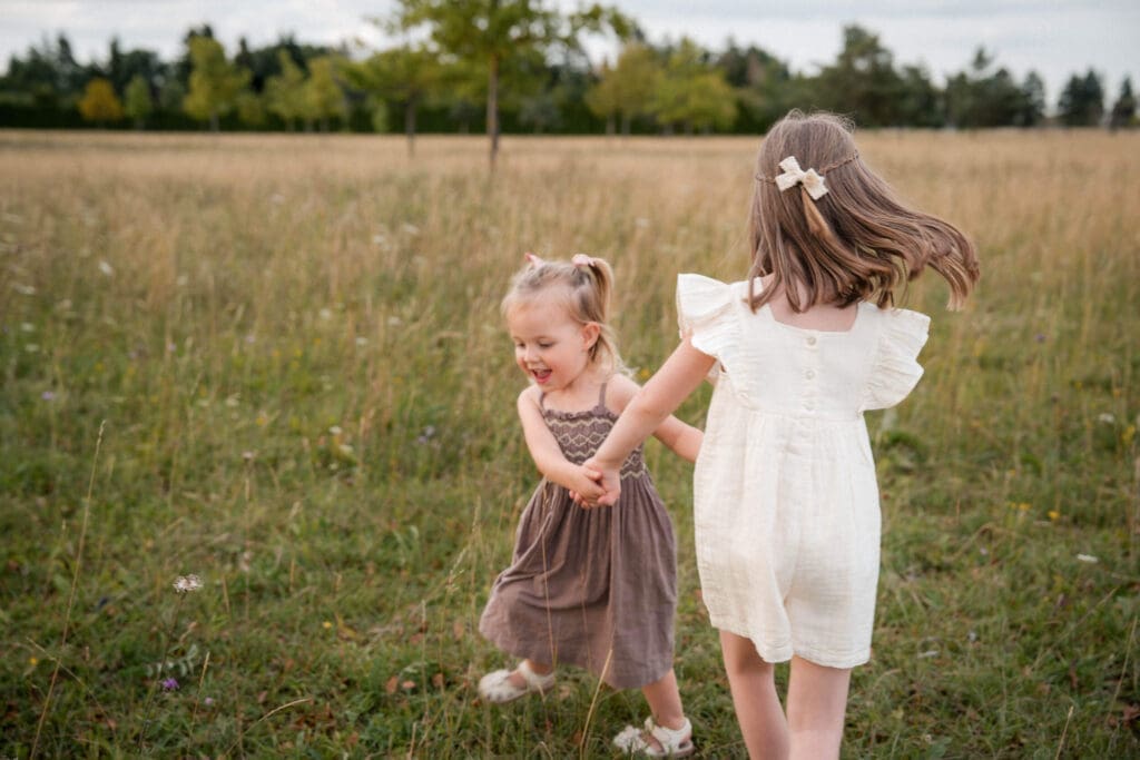 Two little girls hold hands while spinning around in beautiful open field in east Munich.