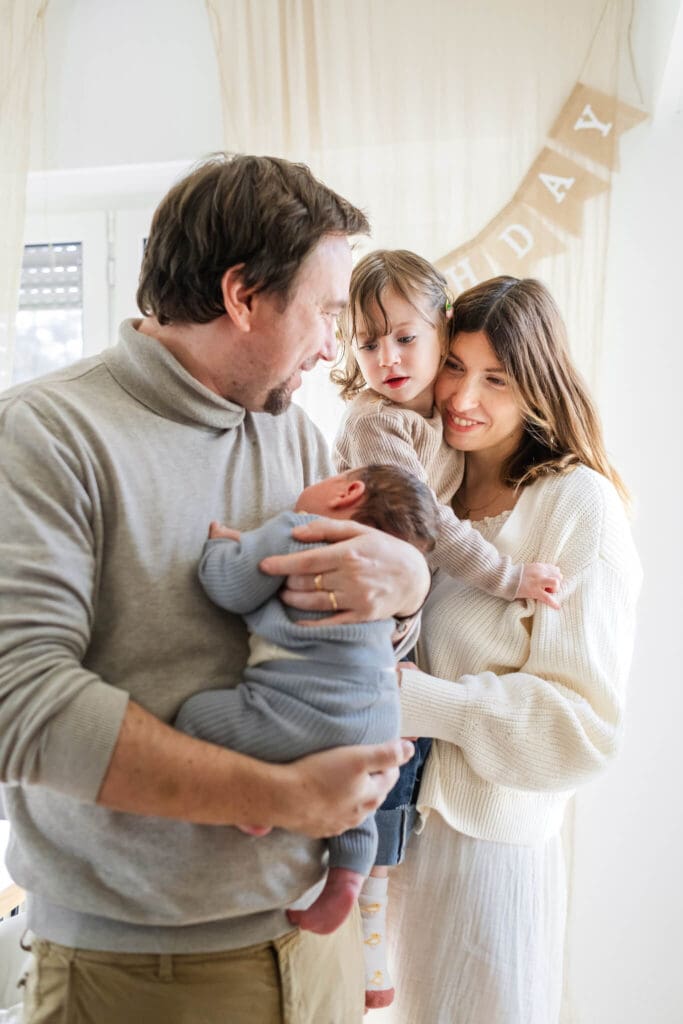 Dad holds newborn and looks back at his wife who is holding a young girl while they look with wonder at the new baby.