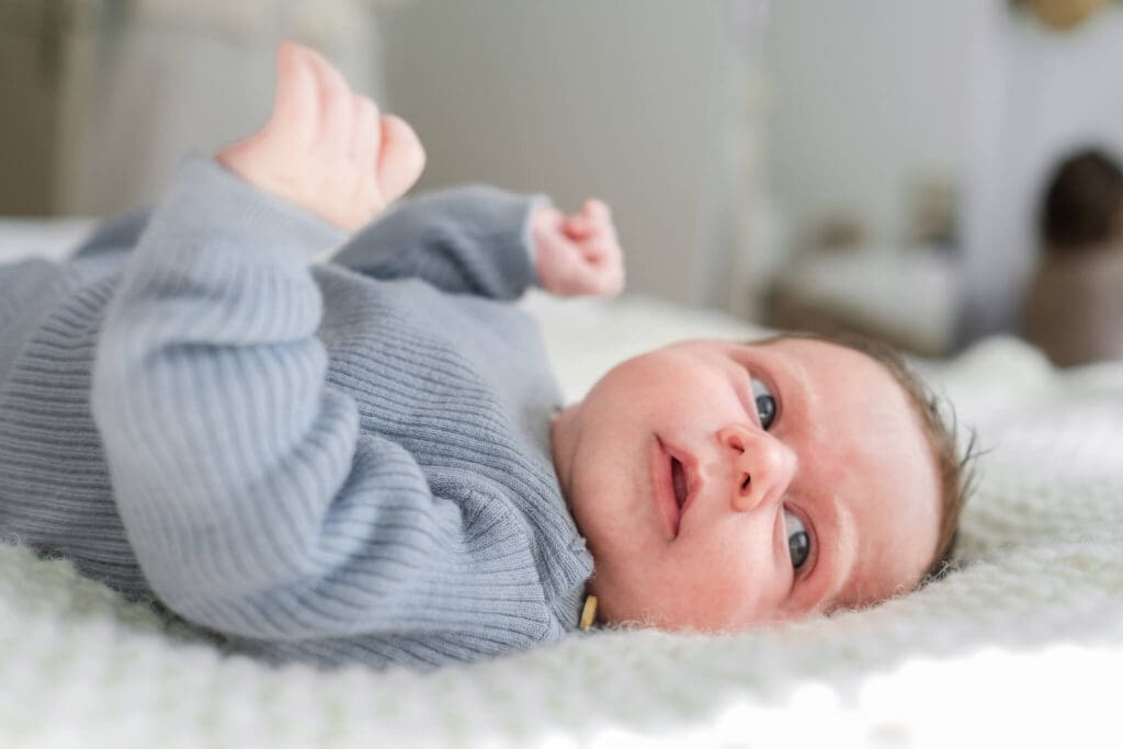 Newborn boy laying on his back and he looks up over his shoulder. His hands flail up while he looks around.
