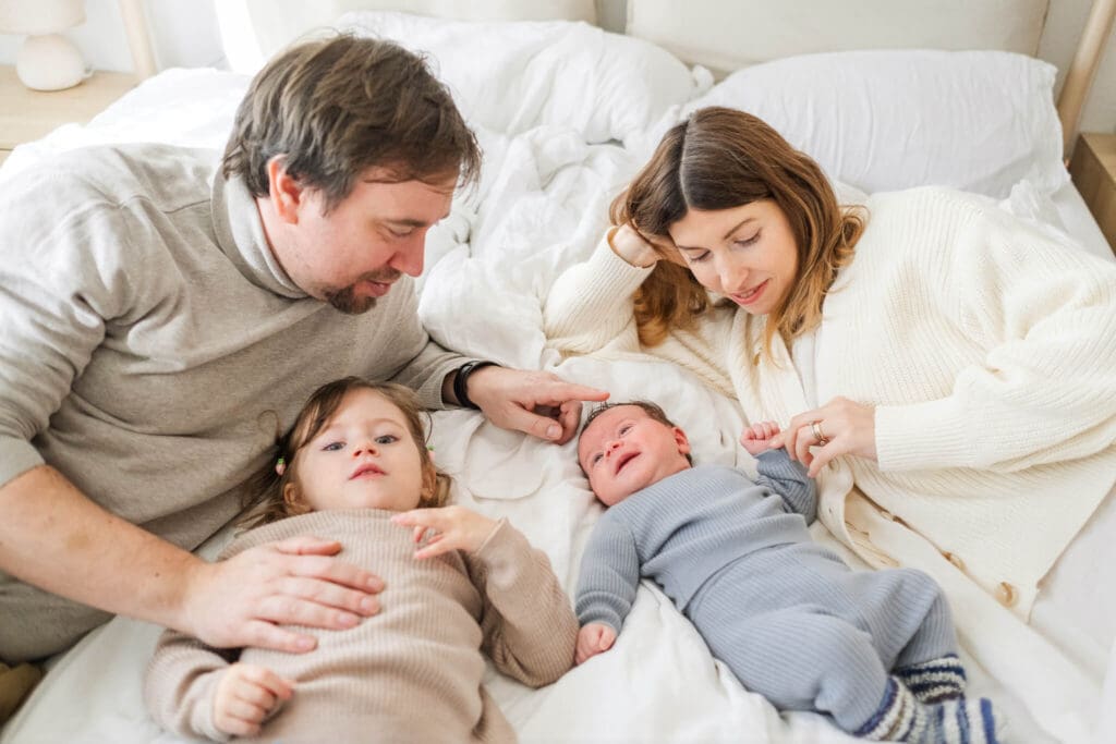 Family of four cuddles in their bed during a newborn homestory session in München-Harlaching
