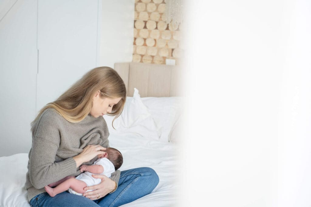 Looking into the room while a mother sitting on a bed with a newborn cuddled on her lap nursing.