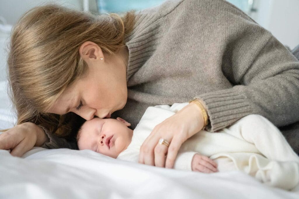 A mother lying next to her sleeping baby, touching noses affectionately.