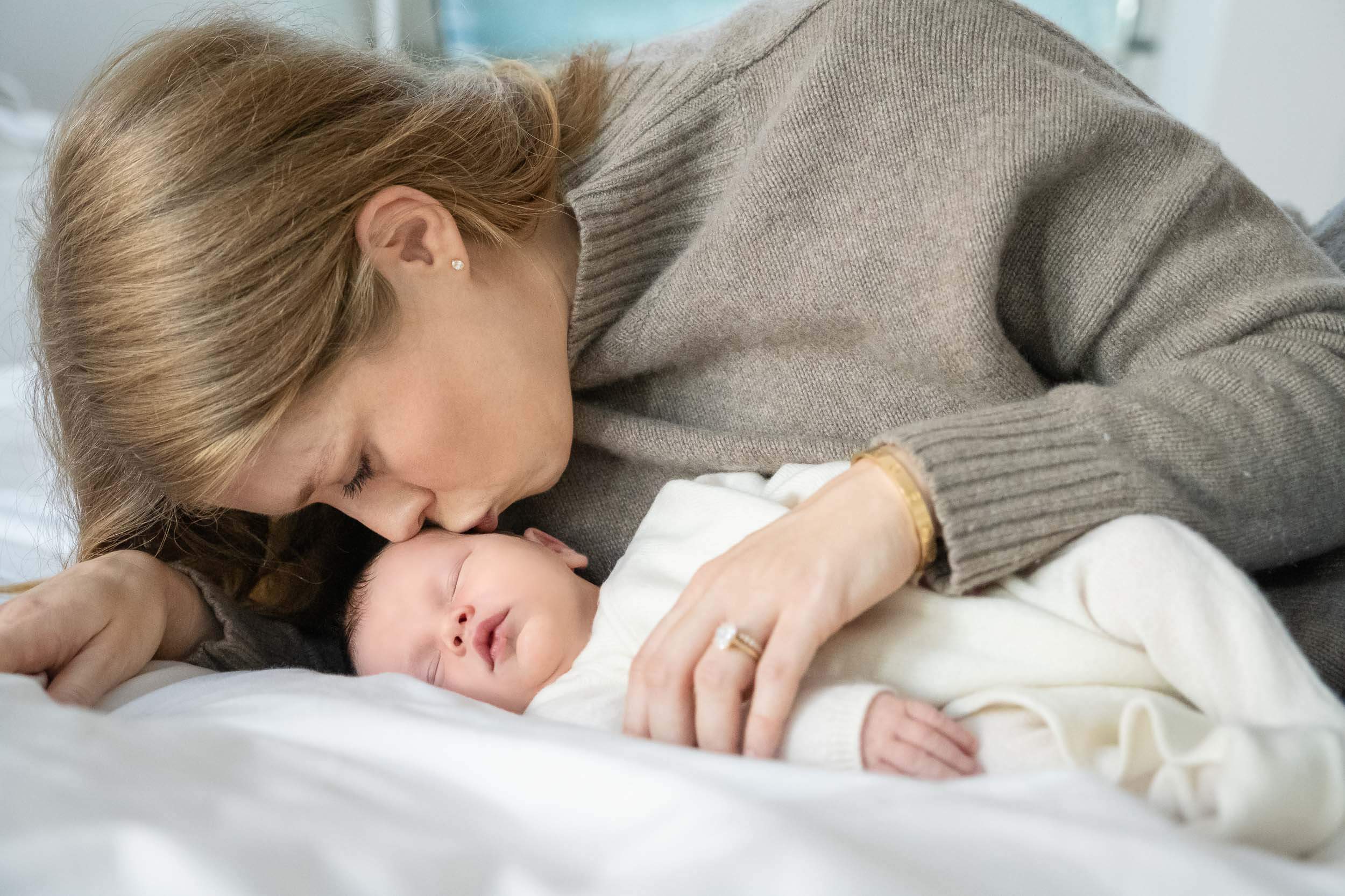 A mother lying next to her sleeping baby, touching noses affectionately.