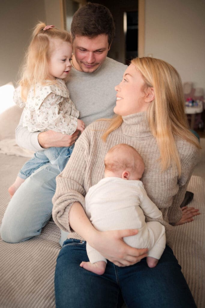 Family of four cuddles together on a couch during a newborn session.