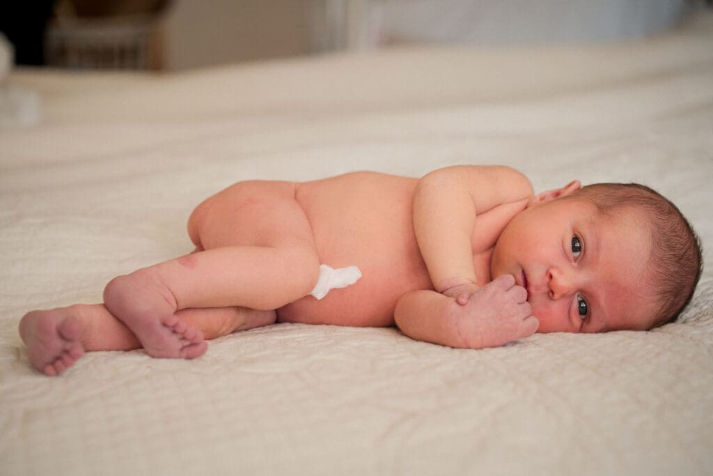 Newborn lays on her side on a cream bedspread.