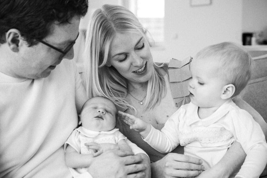 Family sits together as toddler curiously reaches out to touch his newborn brother.