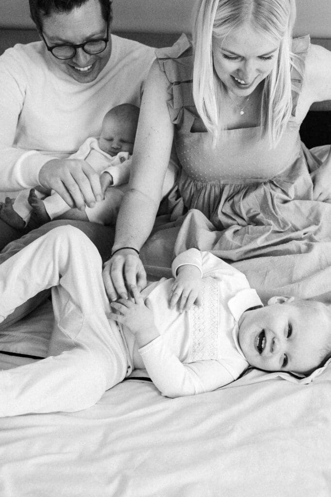 Family with newborn cuddles on the bed together while tickling the older sibling.