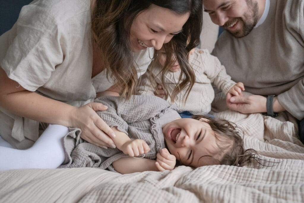 Mother playing with two toddlers on bed during lifestyle photography session in Munich