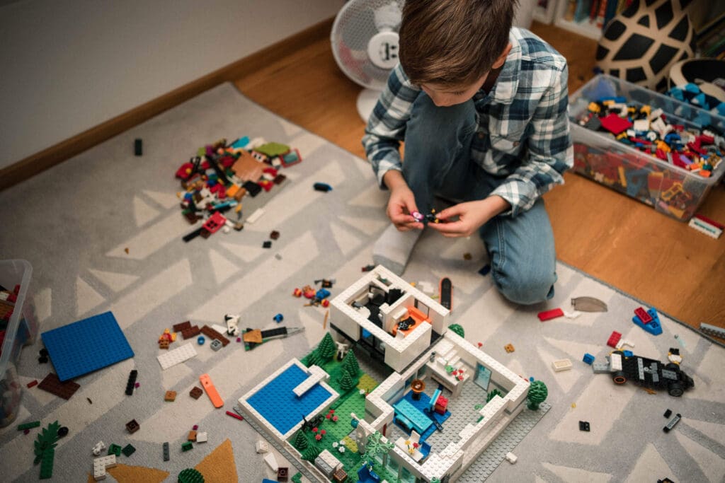 A boy playing with scattered Lego bricks and building blocks on the floor while assembling a construction set.