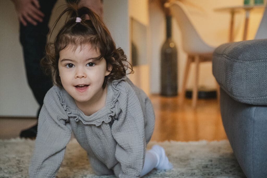 Toddler girl in gray sweater crawls on the floor in natural lifestyle photography moment at home