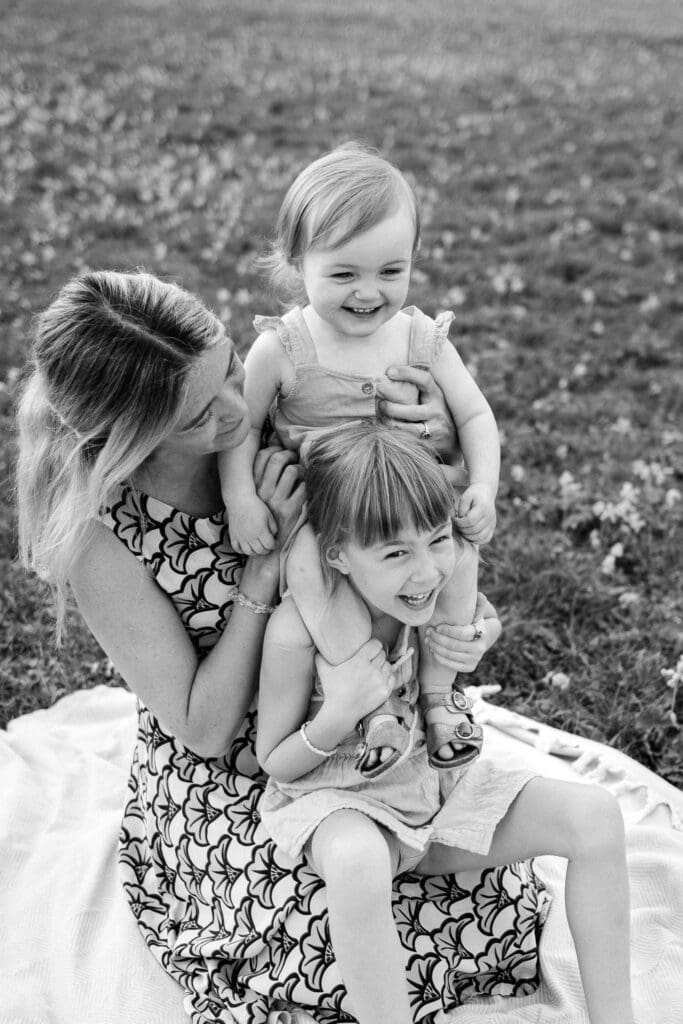 Black and white image of two young girls sitting on their mother's lap laughing.