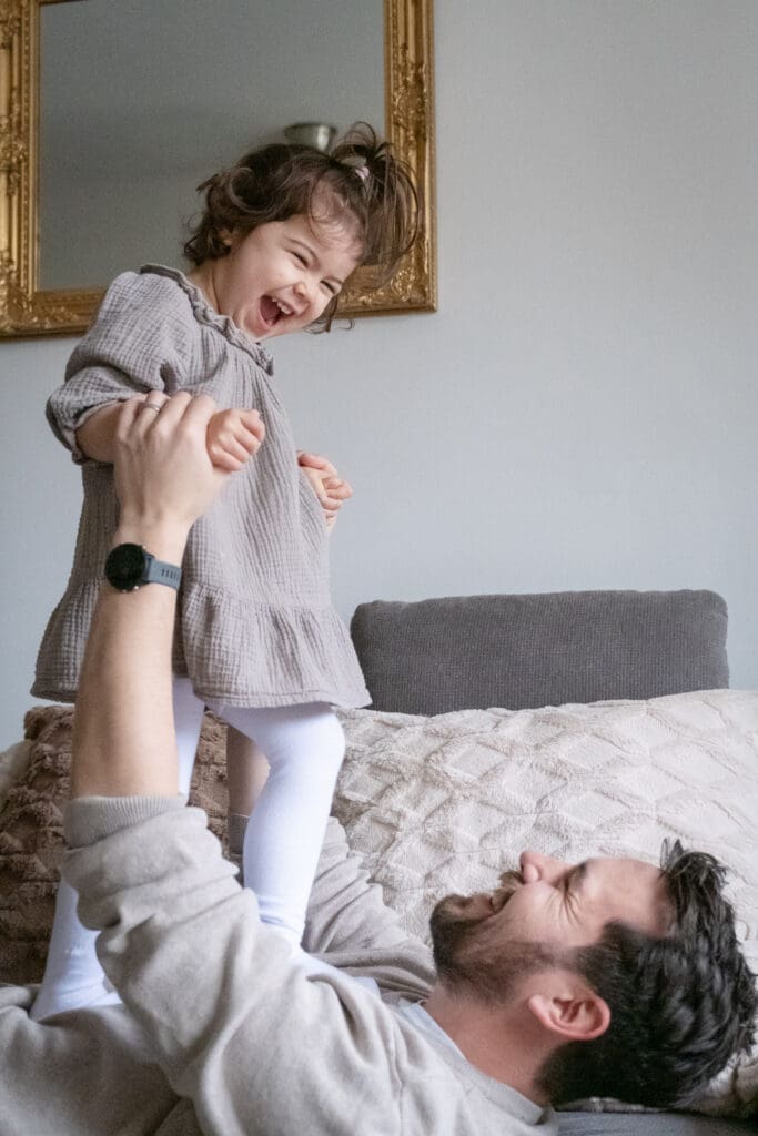 Dad tossing toddler in air during playful family lifestyle photography moment at home