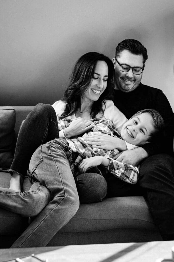 Black and white candid photo of a family laughing together while relaxing on a couch.
