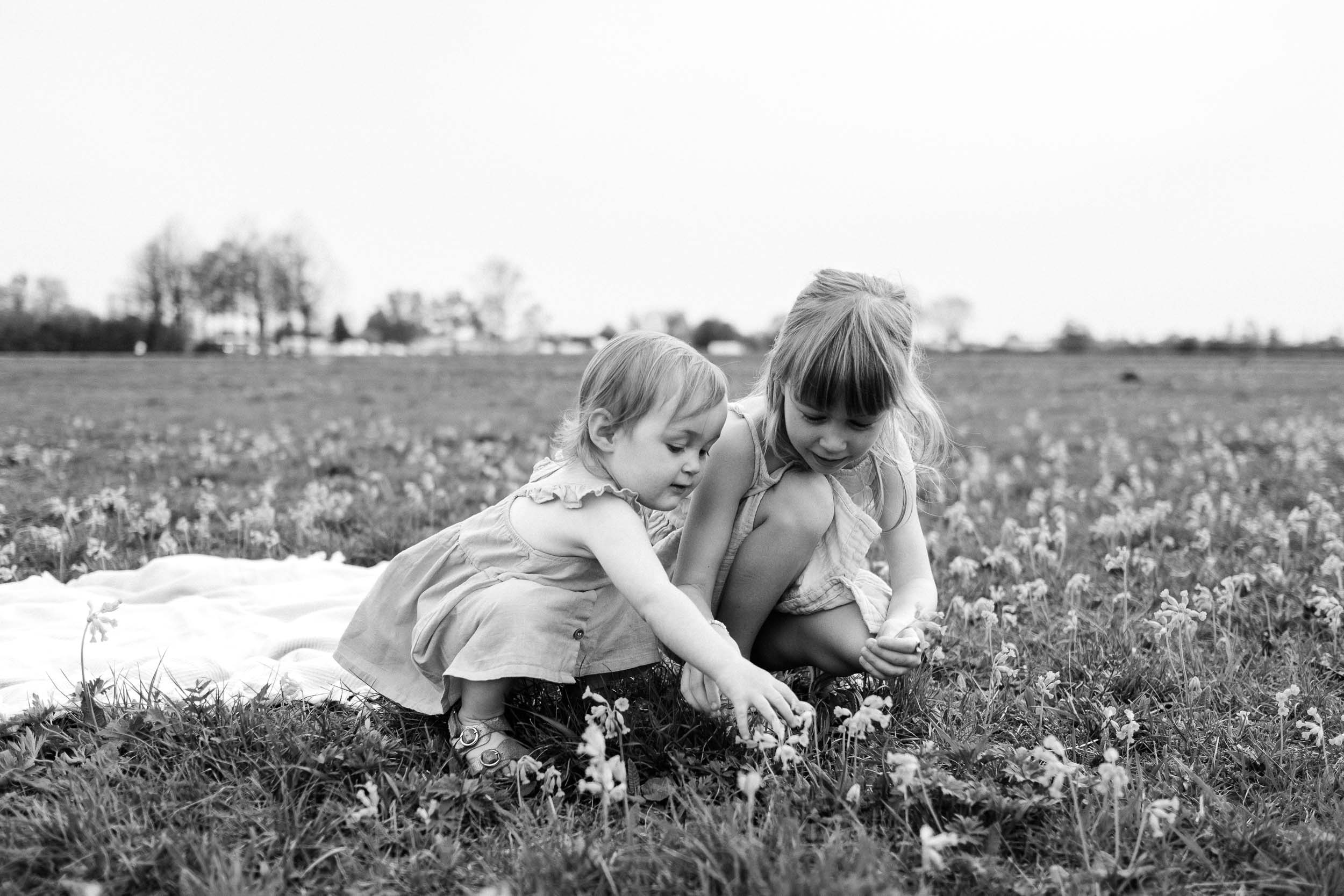 Two young girls look at flowers in meadow