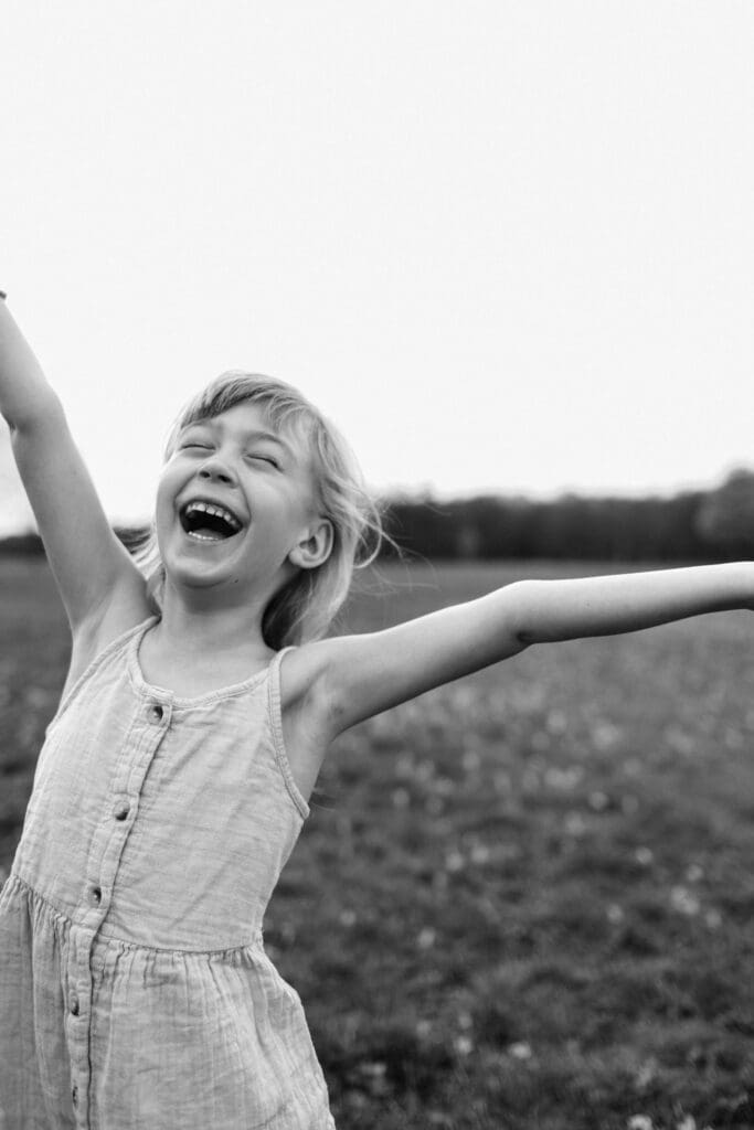 Young girl laughs loudly while throwing her arms up in the air