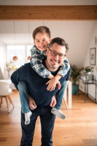 A cheerful piggyback ride takes place in a bright home interior with hardwood floors and modern decor.