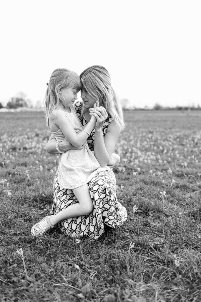 young girl sits on moms knee as they lean in forehead to forehead.