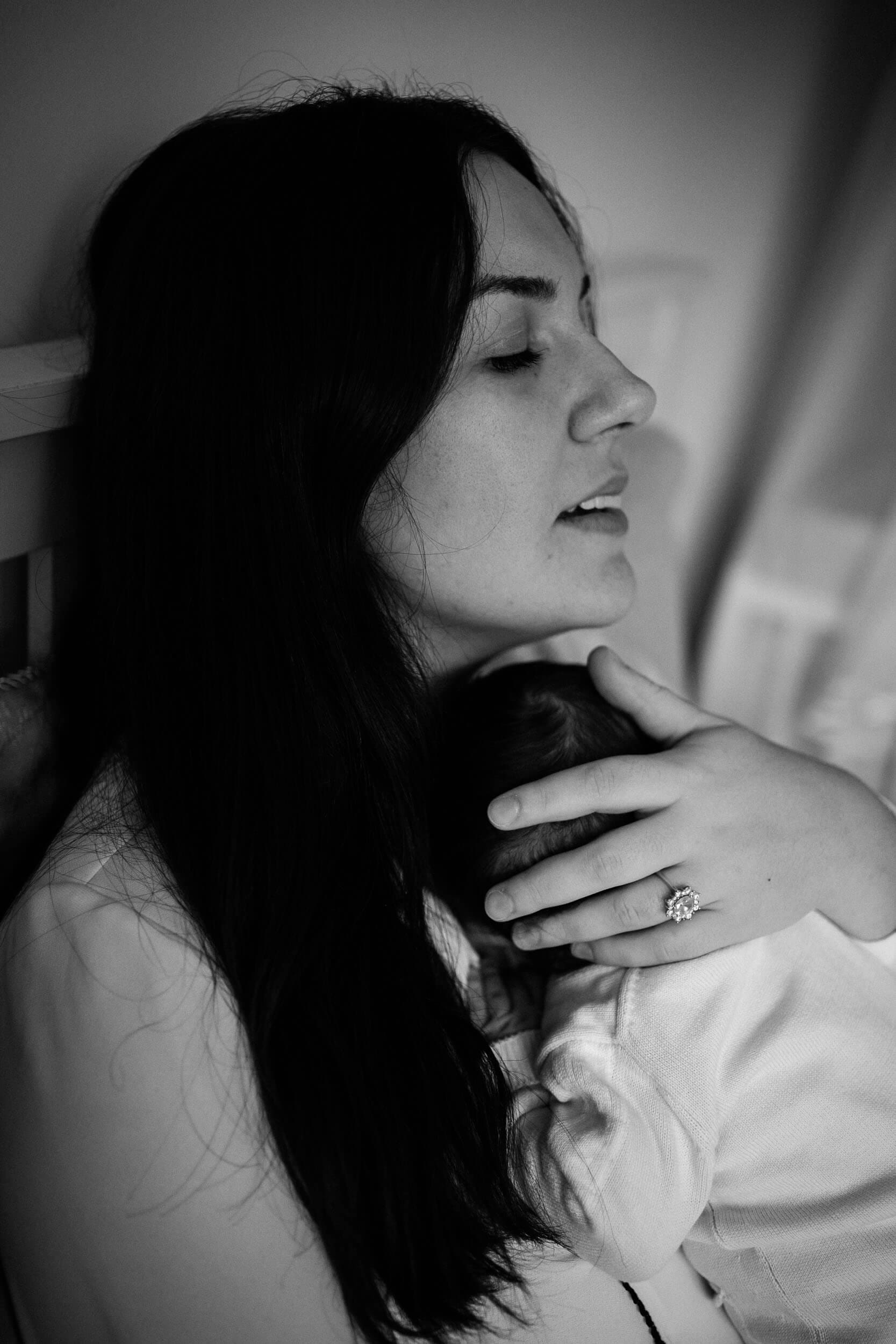 Black and white image of new mother holding her baby close to her chest with her eyes closed.