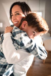 A mom and young boy share a tender moment hugging and laughing together in a sunlit room.