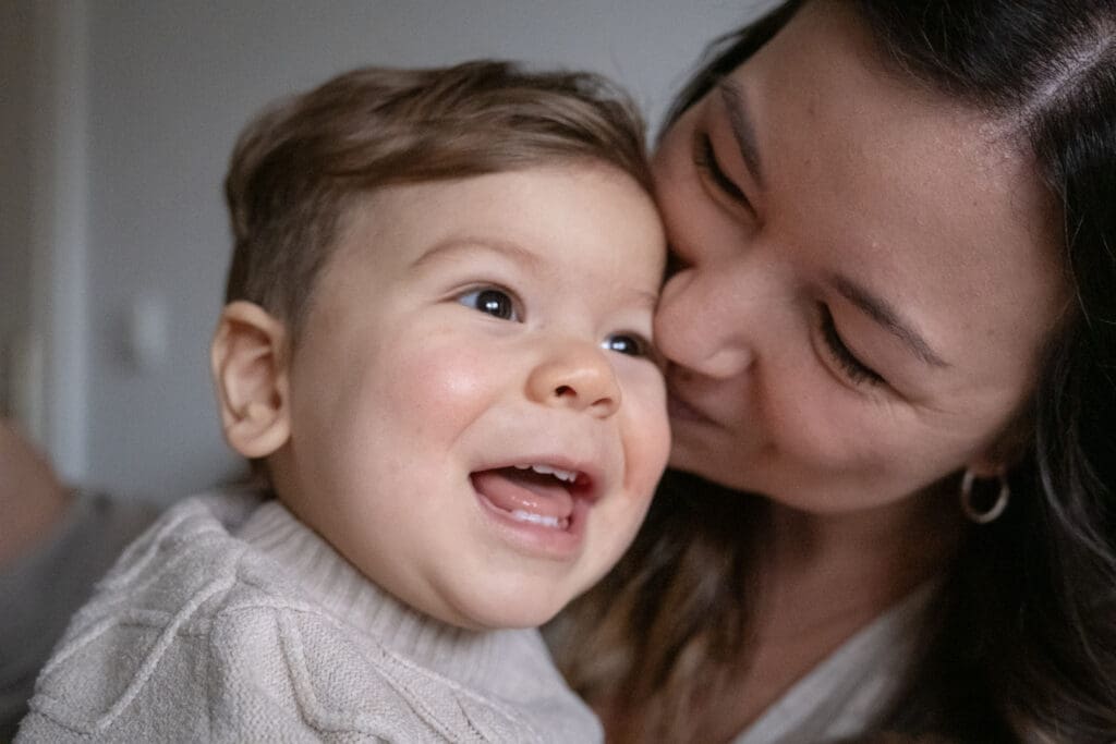Close-up of mother kissing smiling toddler during intimate family lifestyle session"