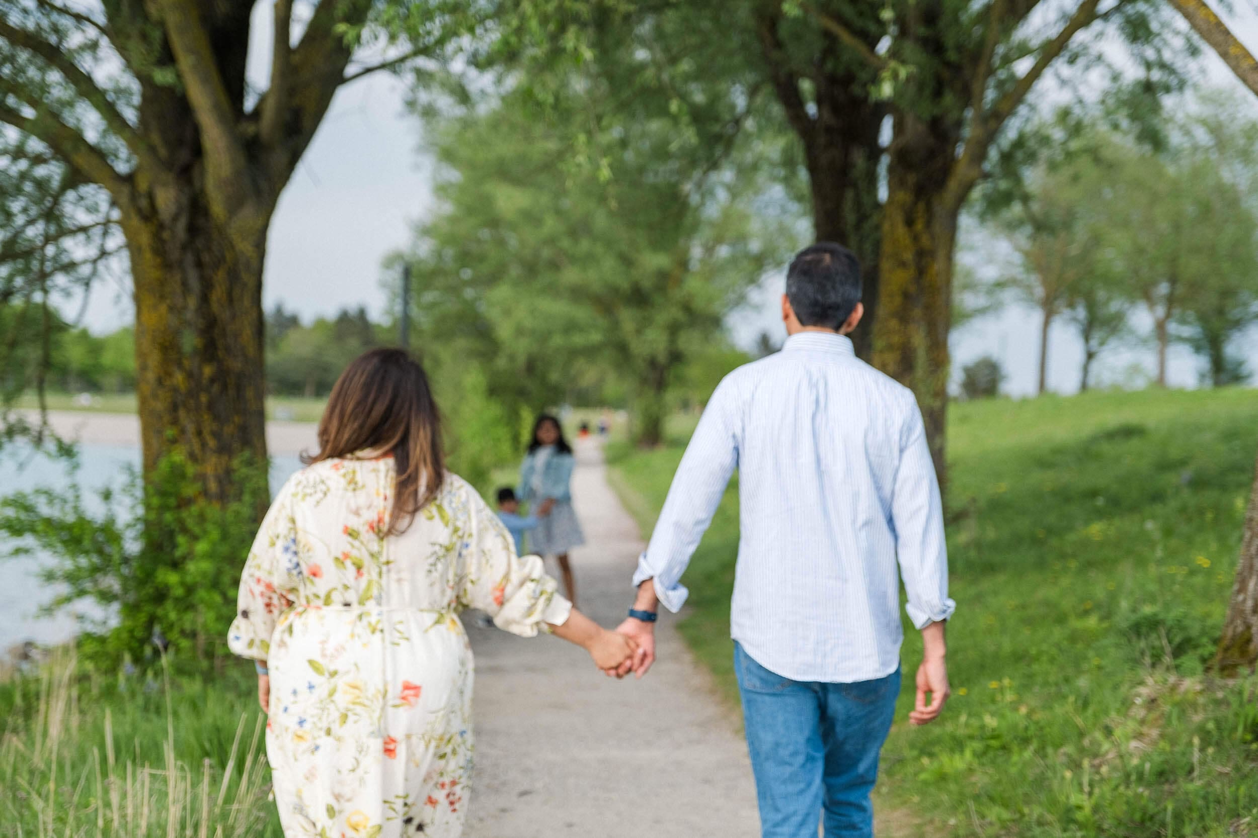 Couple holds hands as the walk along a path next to a Riemersee following their children.