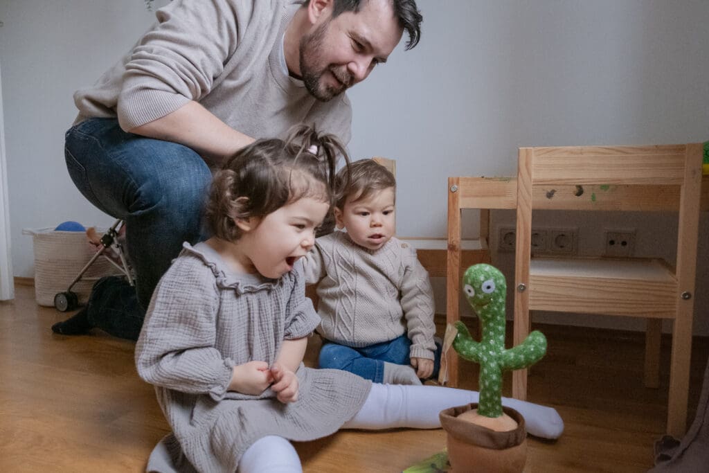 Father playing with two toddlers on floor with cactus toy during authentic family lifestyle photography session