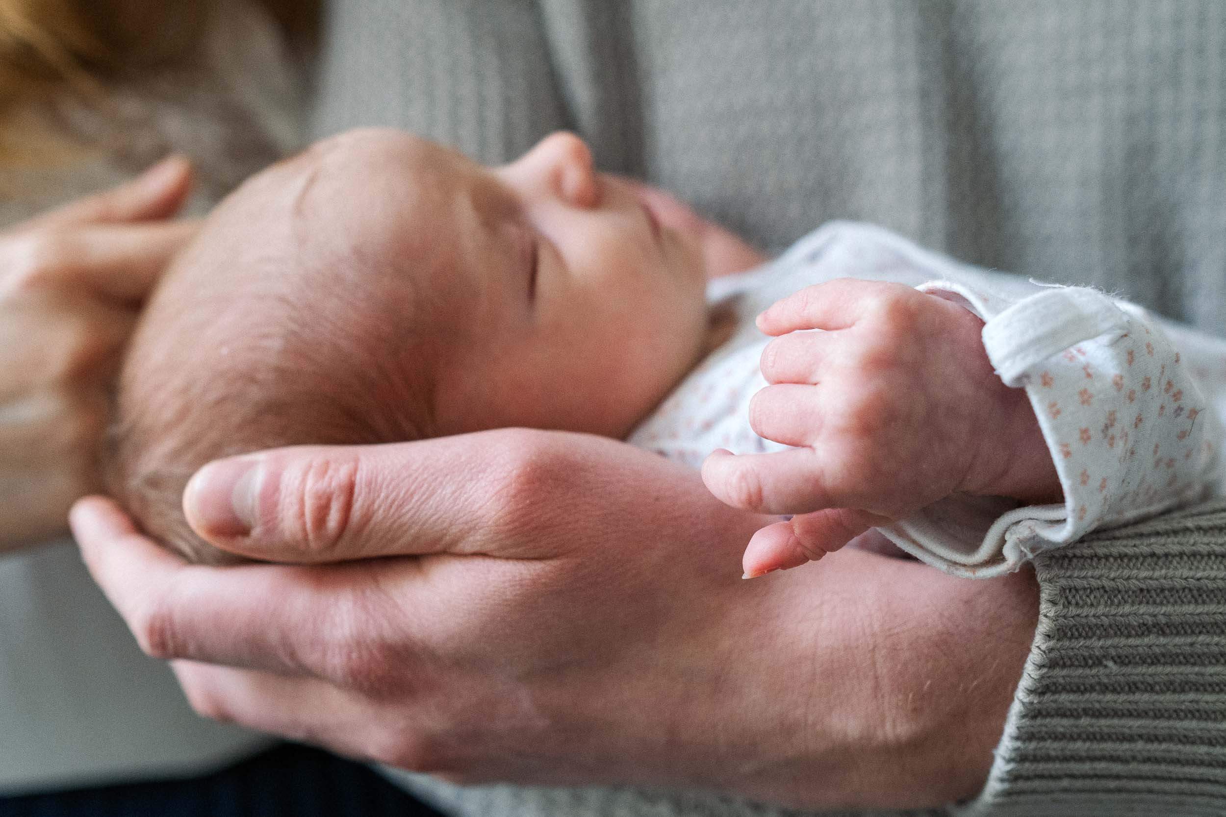 Close-up of a sleeping newborn baby cradled in caring hands.