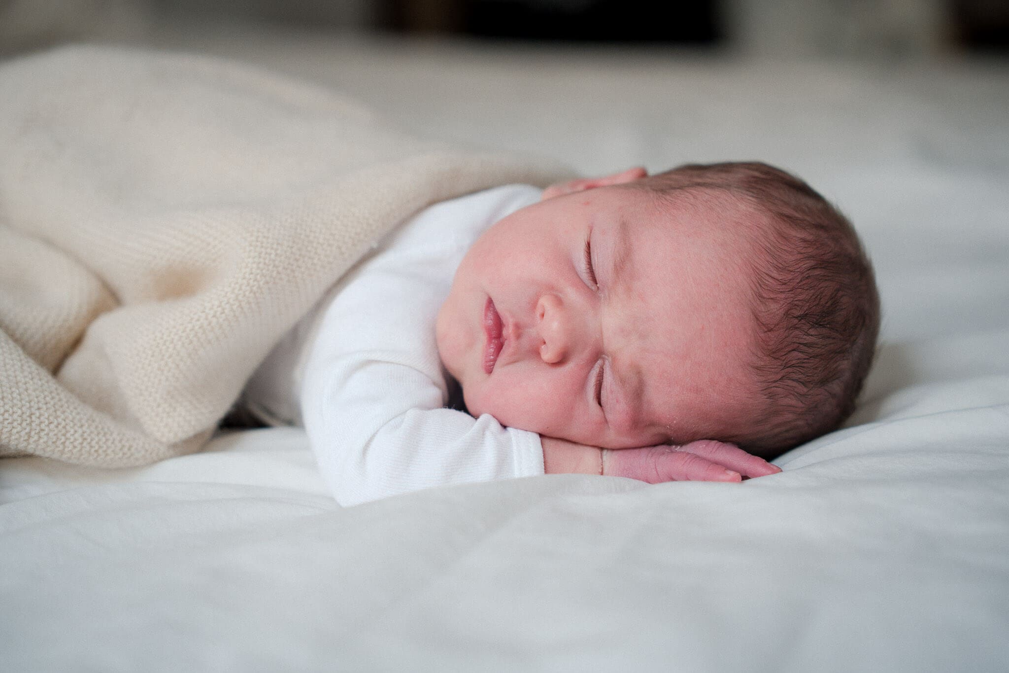 Baby schläft friedlich auf einem weißen Bettlaken während eines entspannten Neugeborenen-Fotoshootings in München.