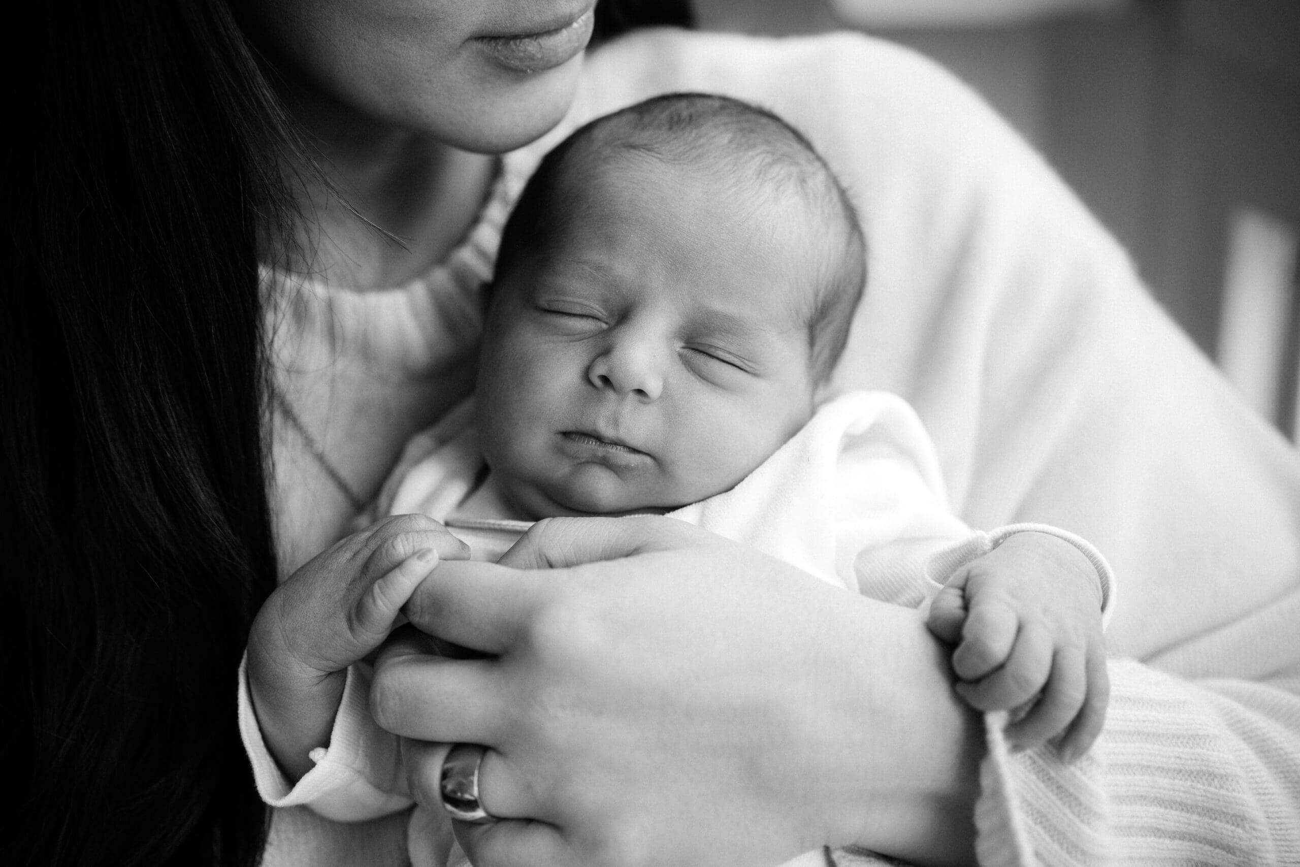 Ein friedliches Neugeborenes schläft in Schwarz-Weiß, während es sanft in jemandes Armen gewiegt wird.