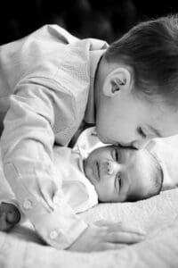 Ein zartes Schwarz-Weiß-Porträt von Geschwistern, die einen intimen Moment miteinander teilen, während sie auf weicher Bettwäsche liegen.