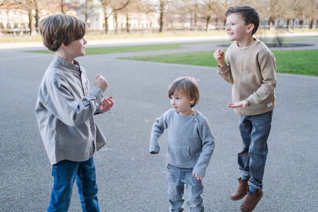 Three boys are playing rock paper scissors while the boy on the far right jumps in excitement.