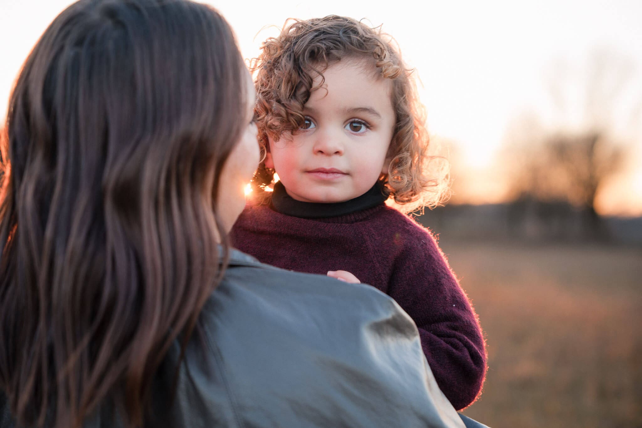 Mother carrying toddler prepared for outdoor family photoshoot at sunset