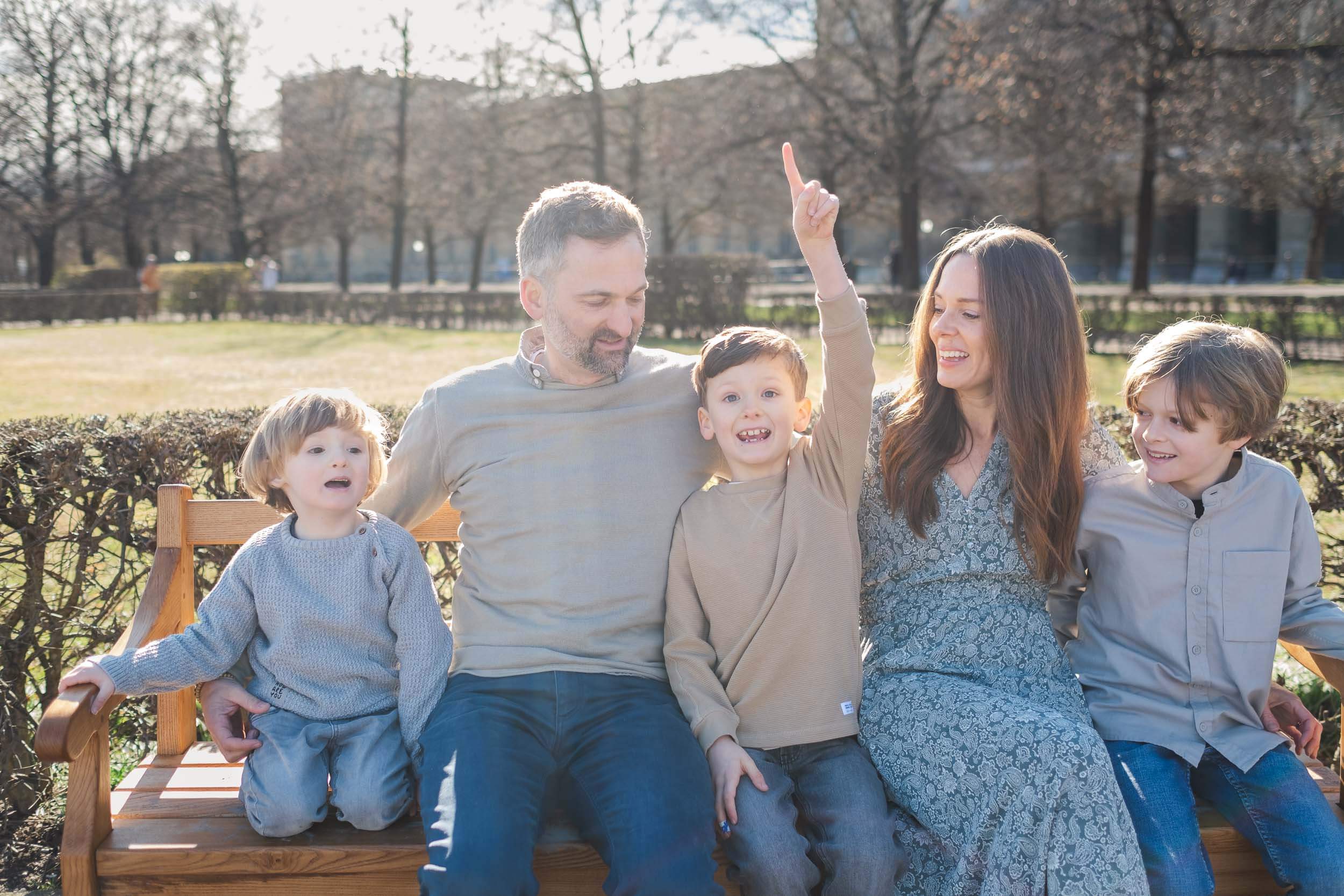 Familie mit drei kleinen Jungen sitzt auf einer Bank, der mittlere Sohn hebt seine Hand