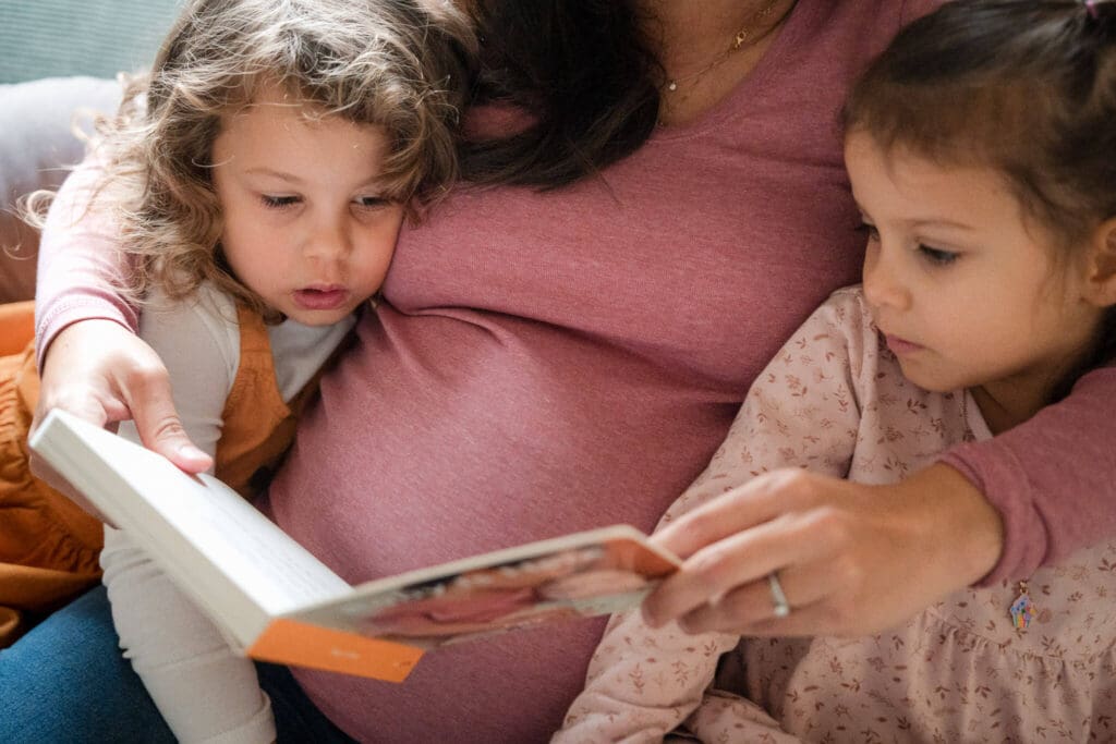 Twin girls snuggle in closely to mom's pregnant belly while she reads them a book.