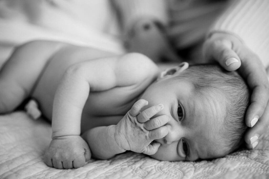 Eine Schwarz-Weiß-Nahaufnahme eines neugeborenen Babys, das liegt und dessen Kopf von erwachsenen Händen sanft gestützt wird.