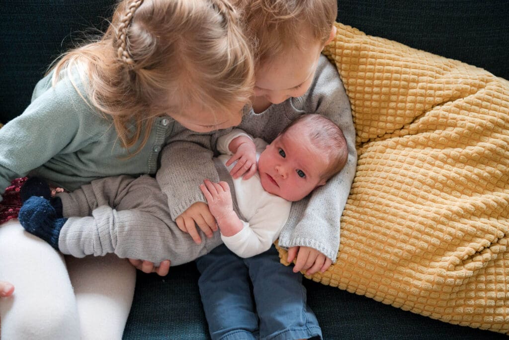 newborn lays on siblibgs lap and looks up during in-home newborn photoshoot in Munich