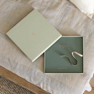 Green linen photo album nestled in a light green storage box laying ontop of a beige cusion