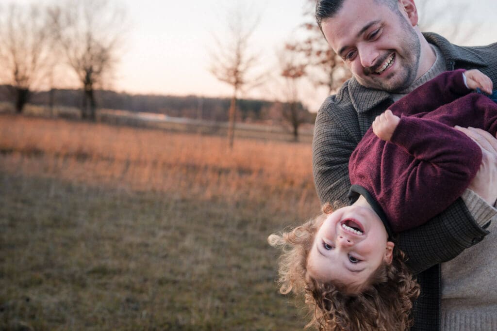 Father dips young boy upside down while they laugh during a sunset family photoshoot