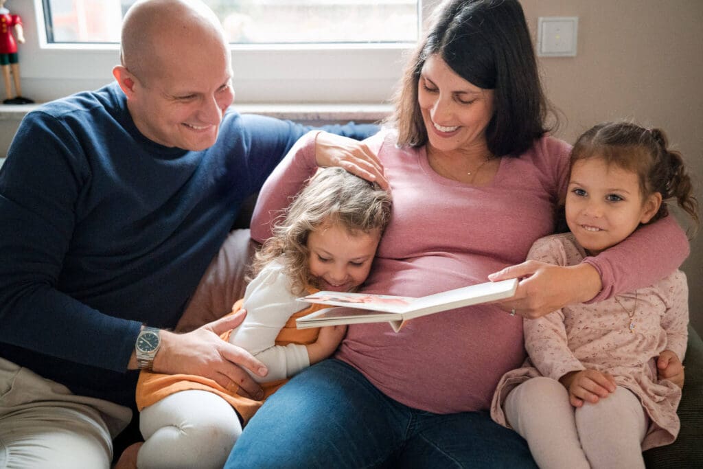 Family of four laughing together on the sofa while reading a book during a lifestyle family photoshoot at home in Munich