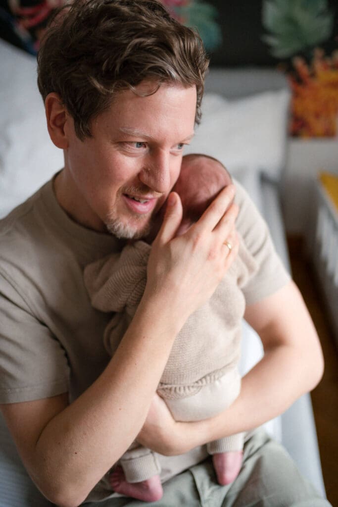 Father snuggles his newborn cheek-to-cheek at home — captured by an English-speaking newborn photographer in Munich