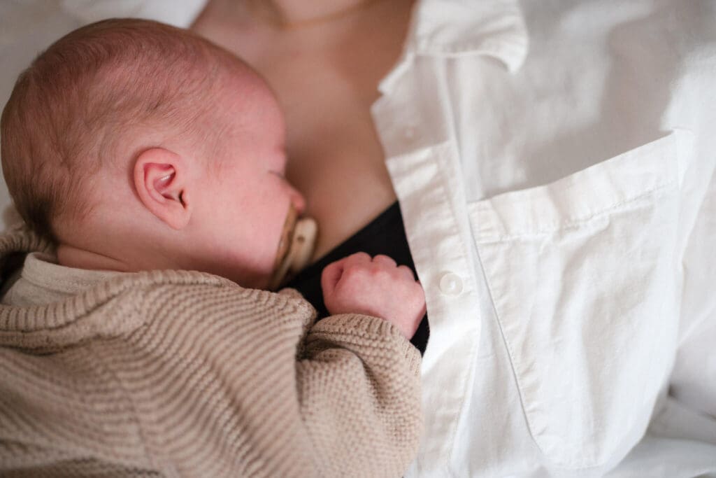 Close-up of a newborn sleeping on mother's chest in a soft beige knit cardigan — an intimate, authentic moment captured without poses.