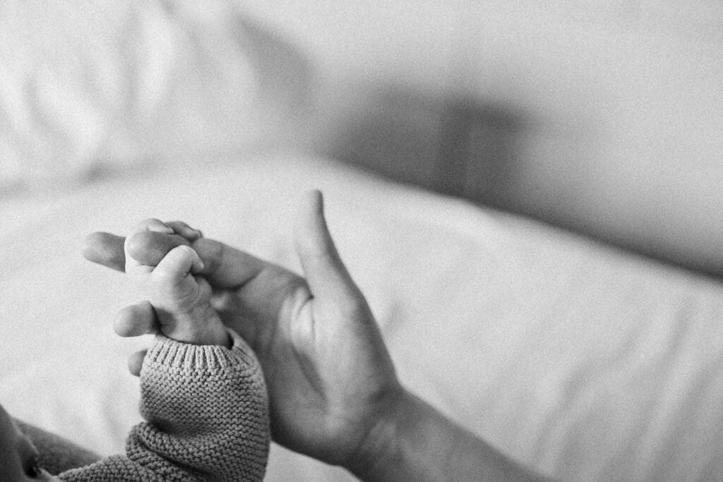 A parent's hand cradles a newborn's tiny grip — a tender black-and-white detail from candid newborn photography in Munich