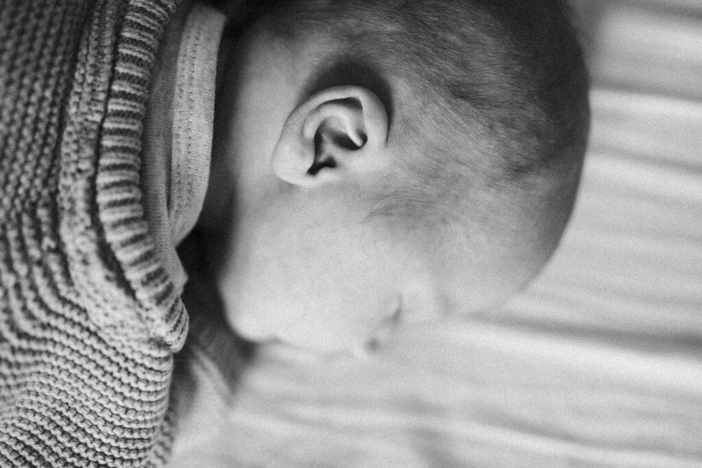 Soft black-and-white close-up of a sleeping newborn's ear and cheek — a quiet moment from a candid Munich newborn shoot
